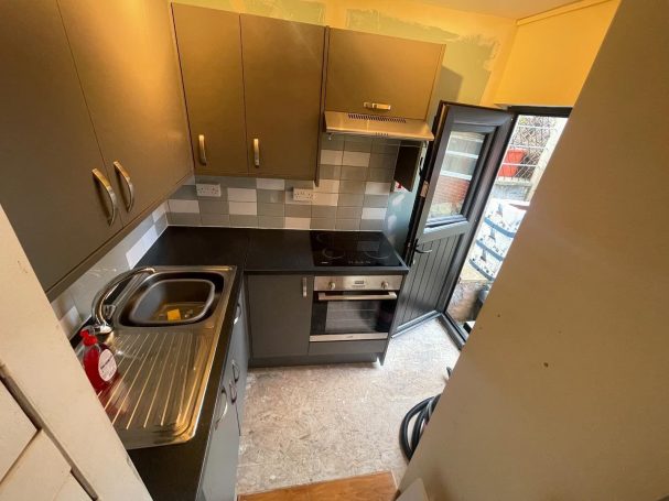 Compact kitchen featuring grey cabinets, stainless steel sink, oven, and fridge.